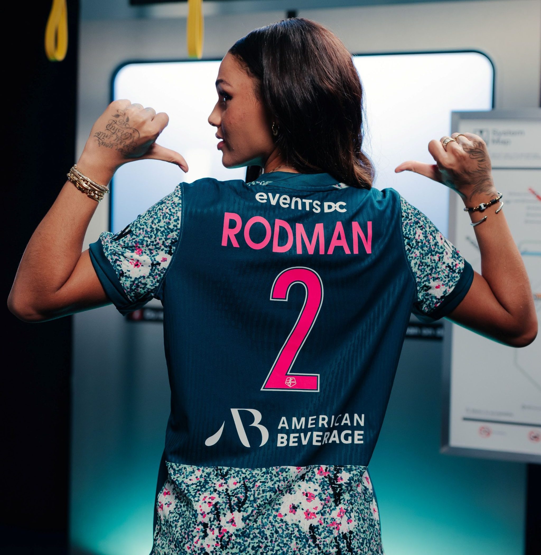 Washington Spirit forward Trinity Rodman stands in a subway car with her back to the camera, thumbs pointing toward her name on the back of her jersey: RODMAN and 2.